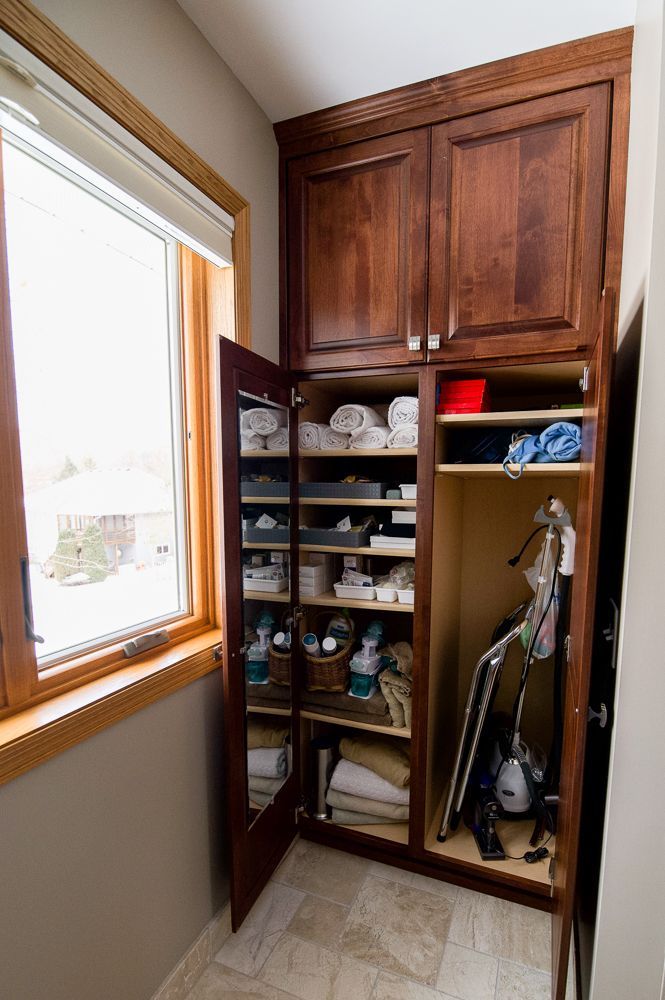 Tall, dark wood cabinet with open doors; towels, supplies on shelves; next to a window.