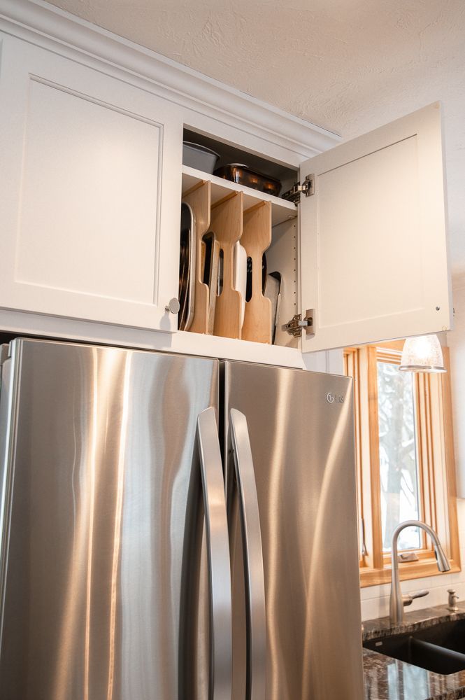 White kitchen cabinets above a stainless steel refrigerator; a utensil holder is inside an open cabinet.