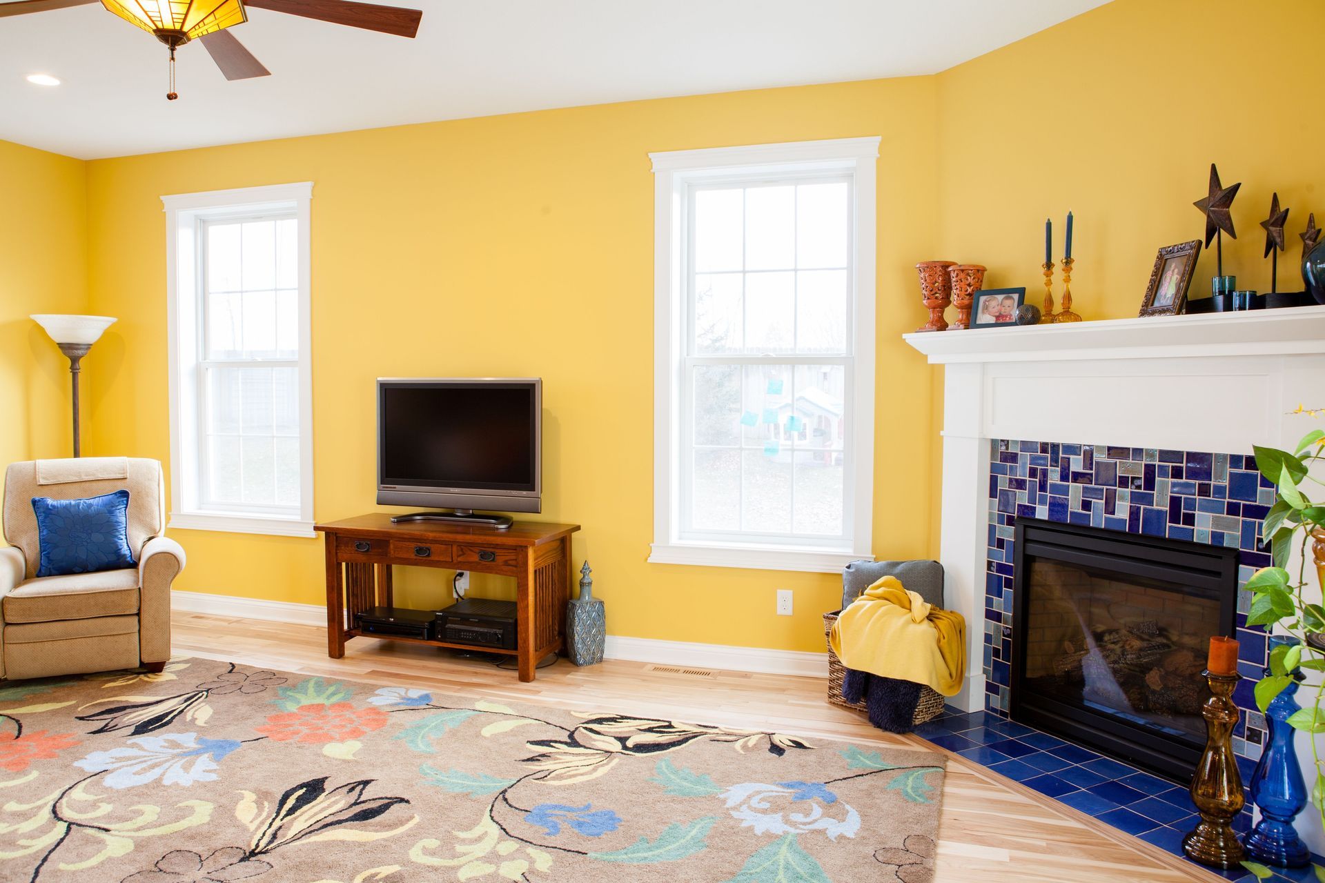 Yellow-walled living room with wood floor, a TV, fireplace, and floral rug.