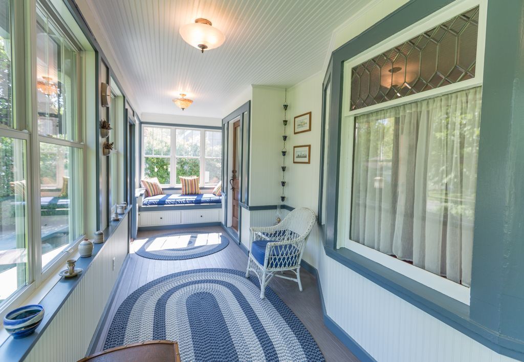 Sunroom with blue and white accents, oval rug, wicker chair, and a built-in window seat.