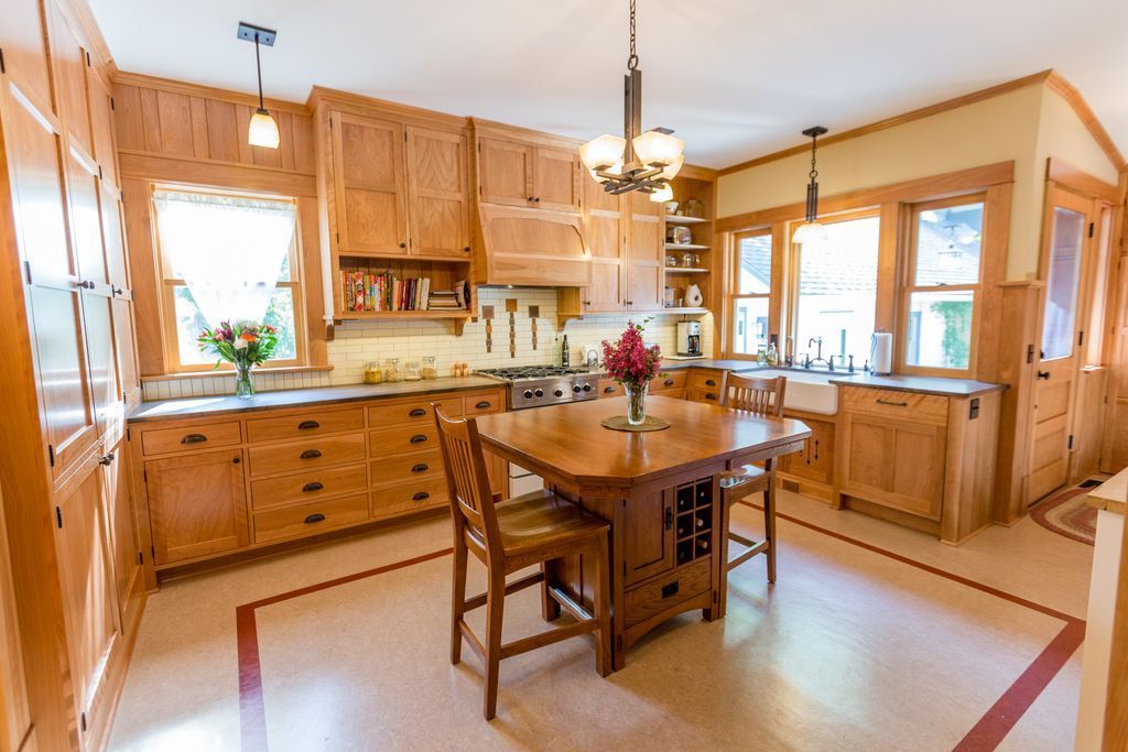 Arts and Crafts style kitchen with light wood cabinets, island table, and red-bordered flooring.