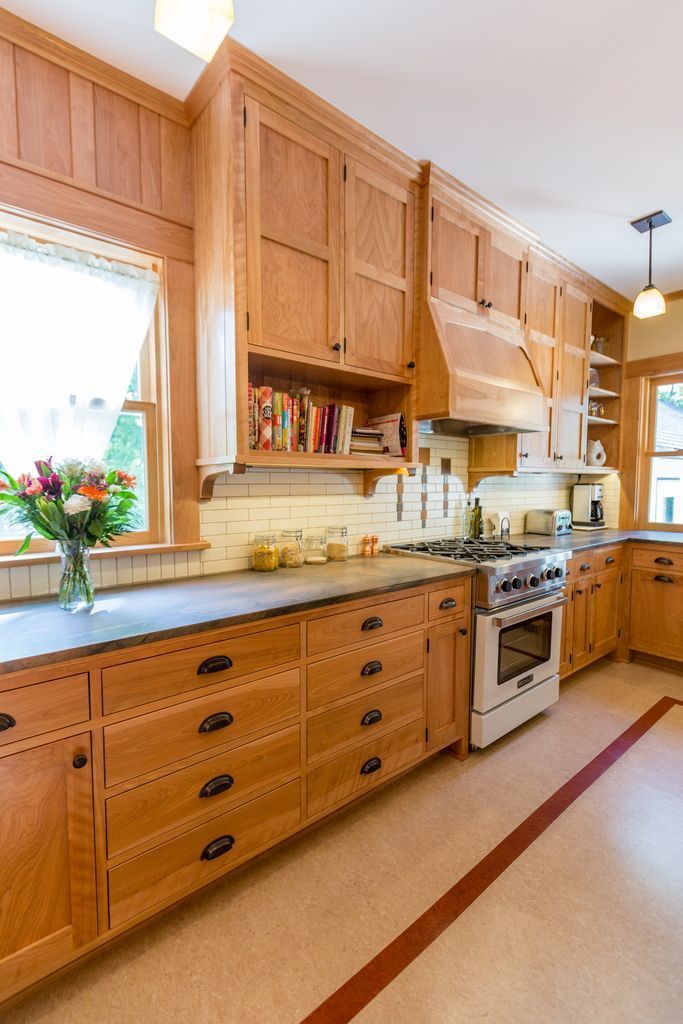 Wooden kitchen with light cabinets, a stove, and a window with flowers.