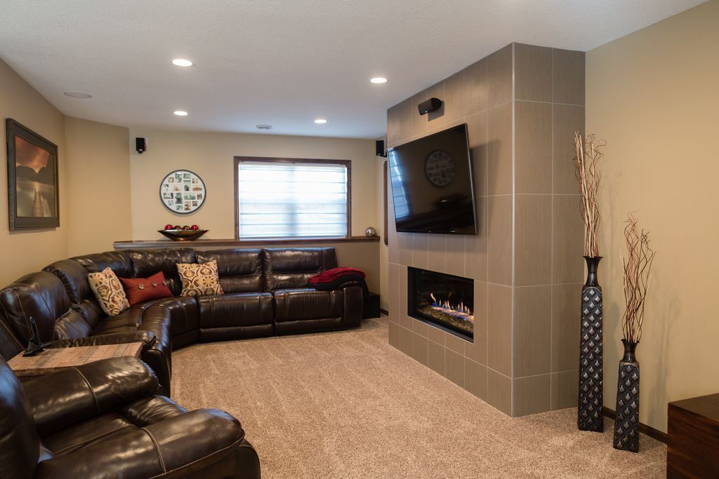A brown leather sectional sofa in a finished basement with a fireplace, tv, and vases.