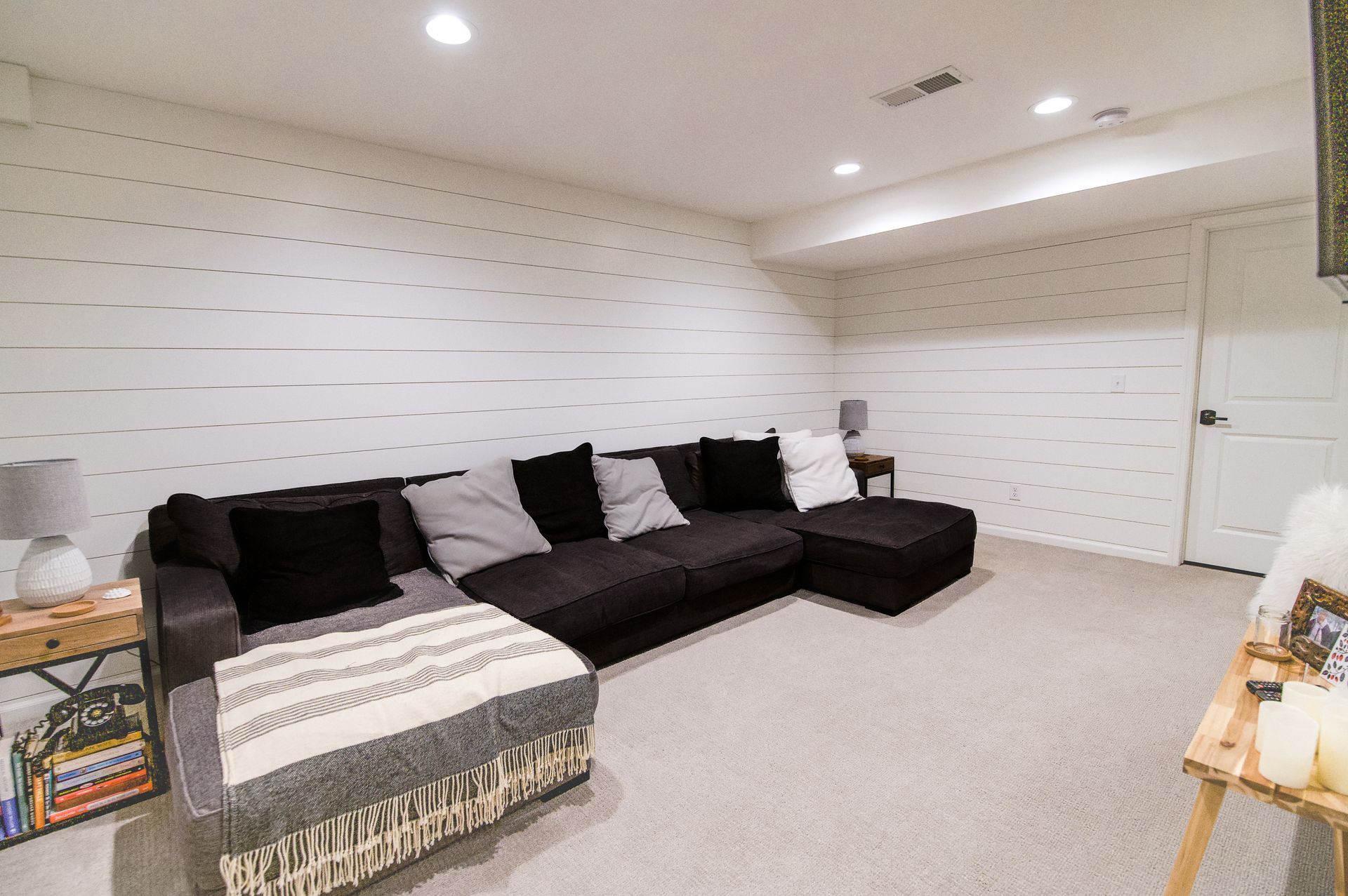 A dark sectional sofa in a white-walled room with shag carpet; side tables with lamps, doorway.