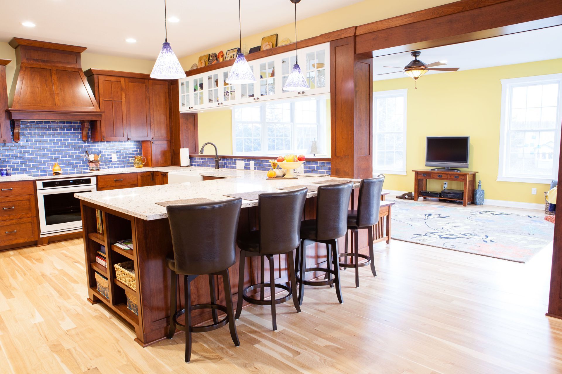 Kitchen with wood cabinets, large island with stools, and yellow wall in the background.