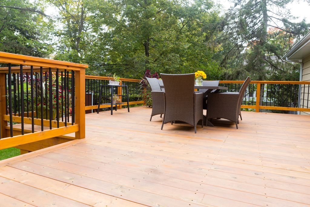 Wooden deck with a dining set; black railing, trees in the background.