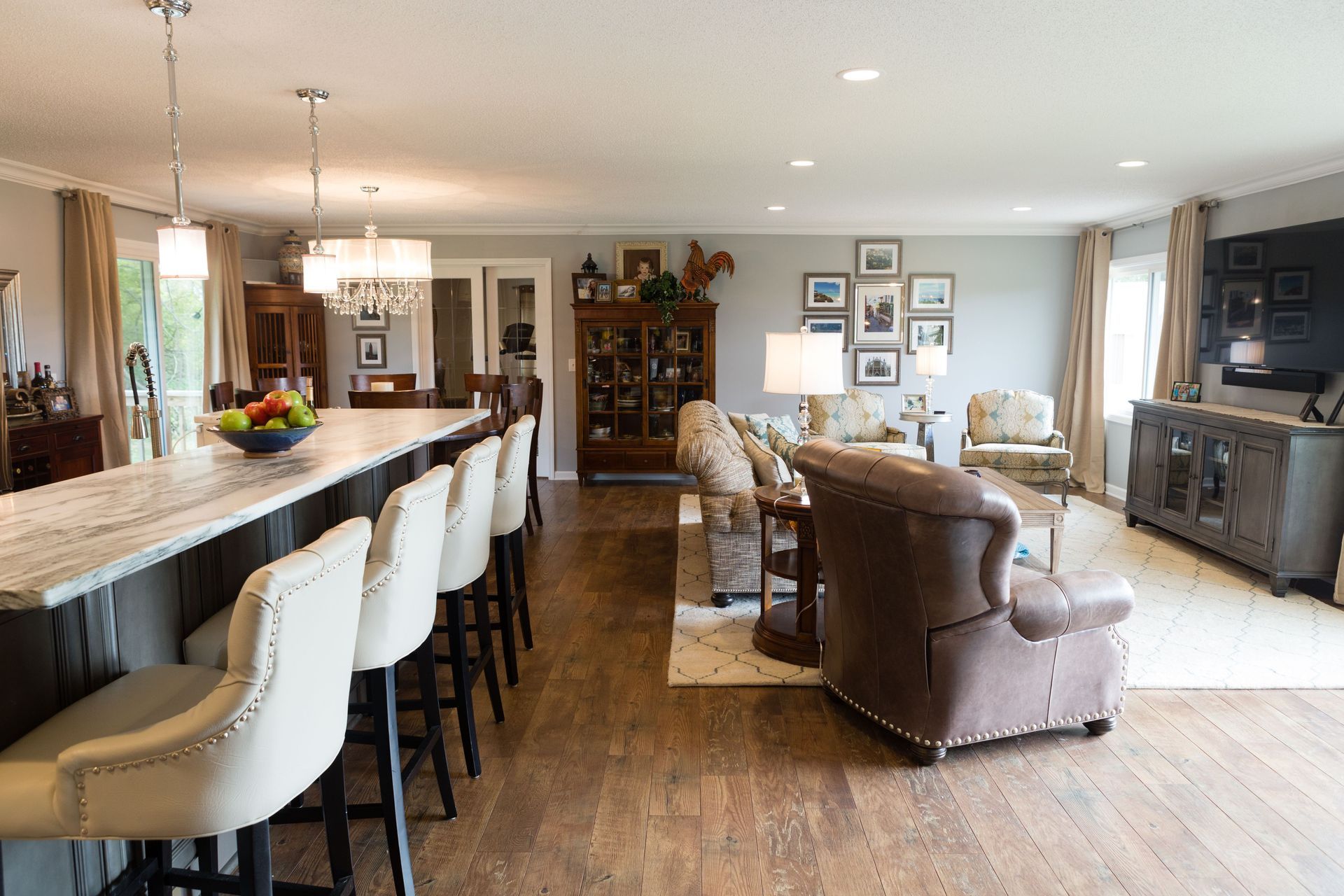 Open-concept living space with a kitchen island with barstools, living area with a TV, and hardwood floors.
