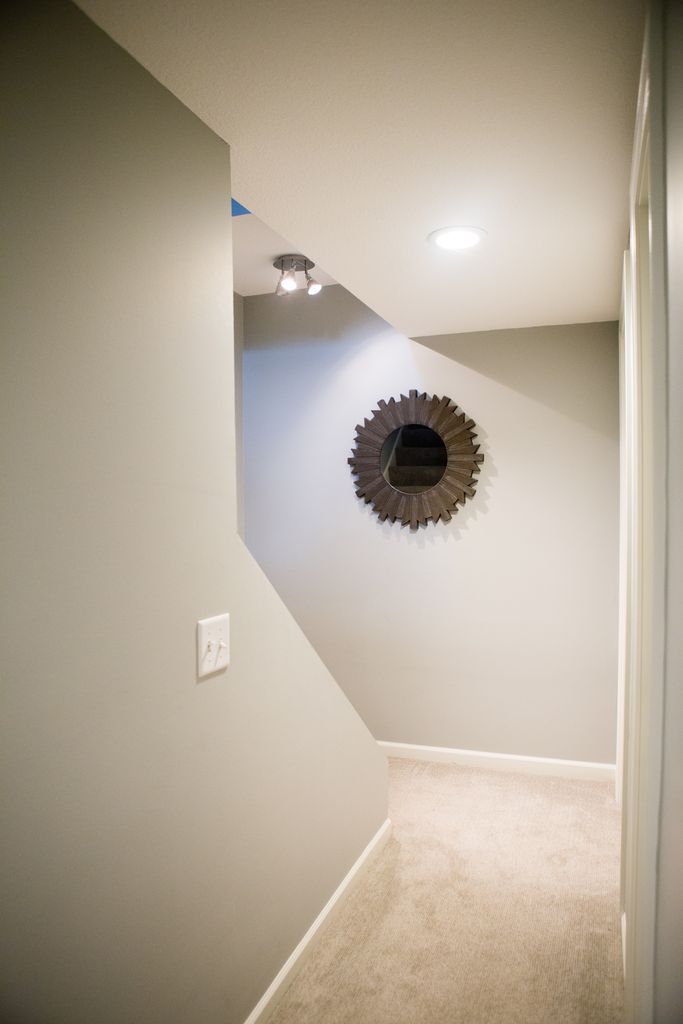 Narrow hallway with staircase leading down, light gray walls, and decorative mirror.