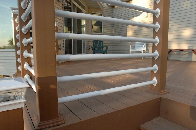 Wooden deck with brown posts, white railing, and view of a house through sliding doors.