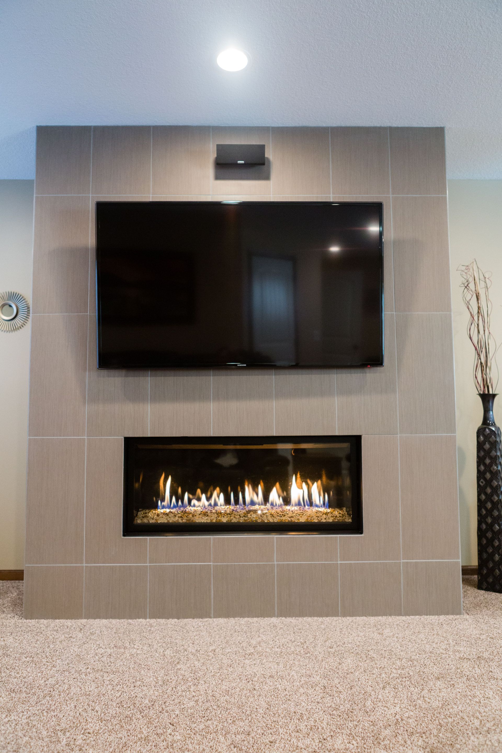 Fireplace with a mounted TV, framed in gray tiles, set against a neutral-toned wall.