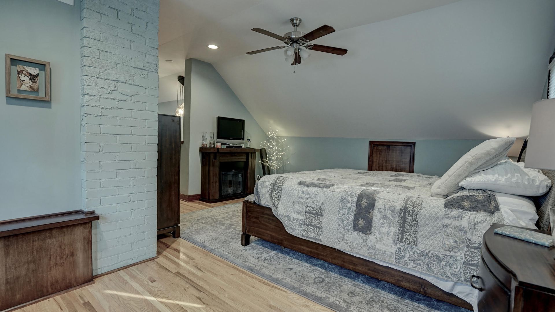 Bedroom with light blue walls, hardwood floor, and a bed with a patterned comforter.