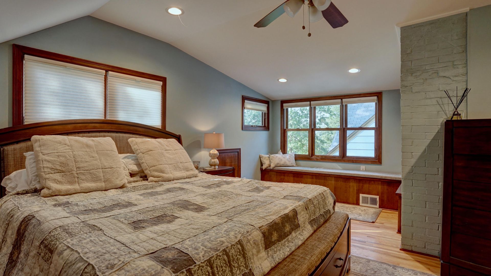 Bedroom with large bed, window seat, and vaulted ceiling; light blue walls.