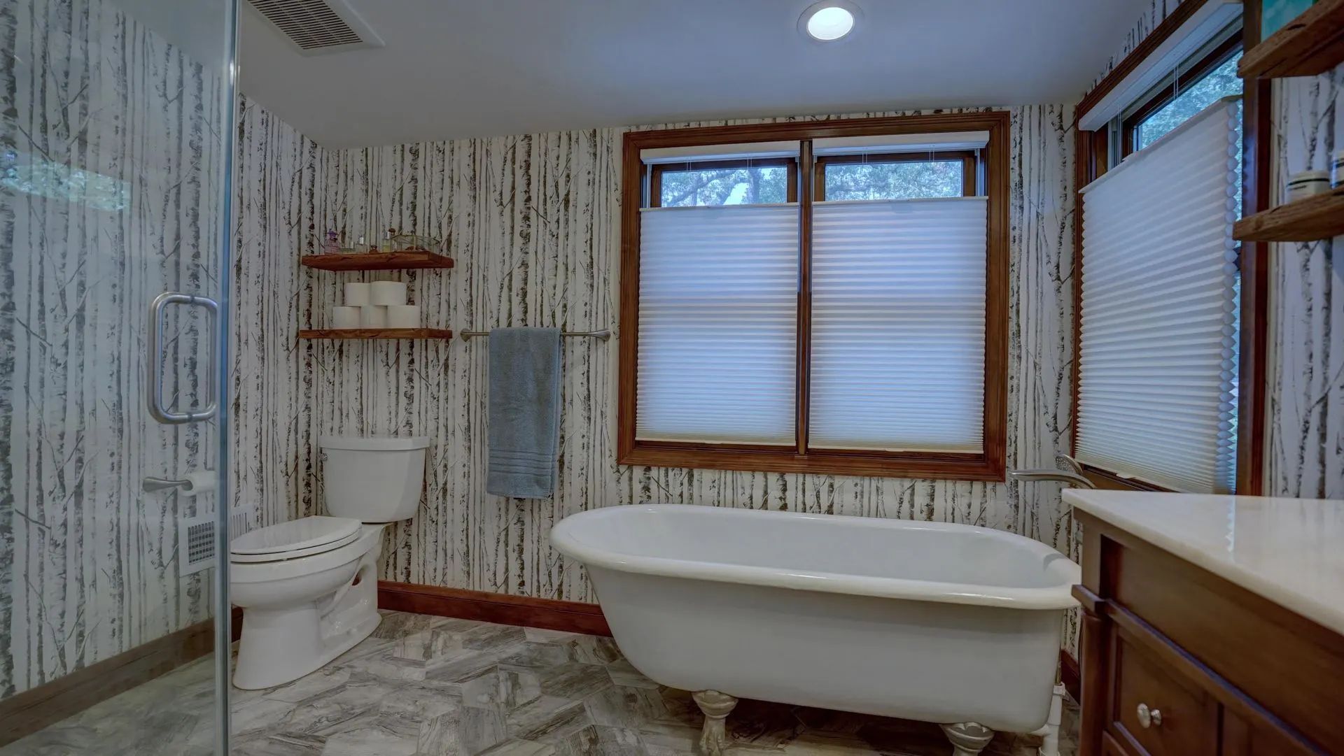 Bathroom with clawfoot tub, toilet, shower, wooden-framed window, and textured wallpaper.