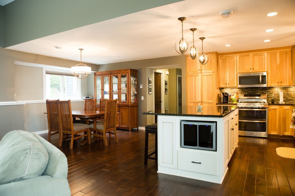 Kitchen with wood cabinets, island with microwave, dining area with wood table, and dark hardwood floors.