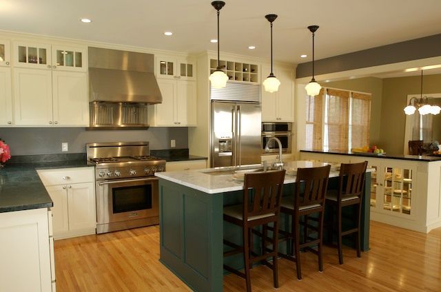 Spacious kitchen with a green island, stainless steel appliances, and pendant lights over wooden floors.