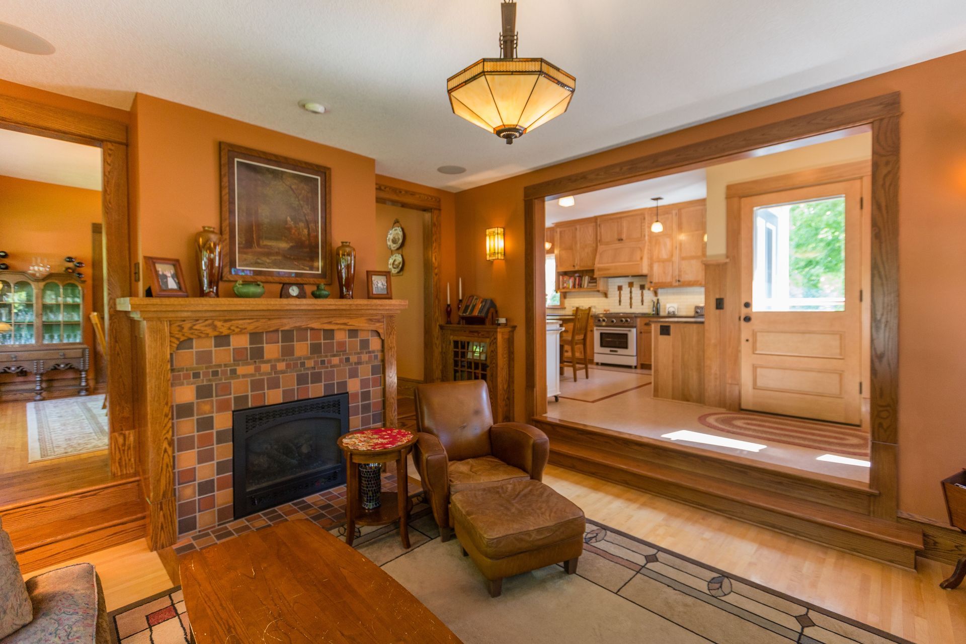 Living room with fireplace and doorway to kitchen. Orange walls, wooden trim, and a chaise lounge.