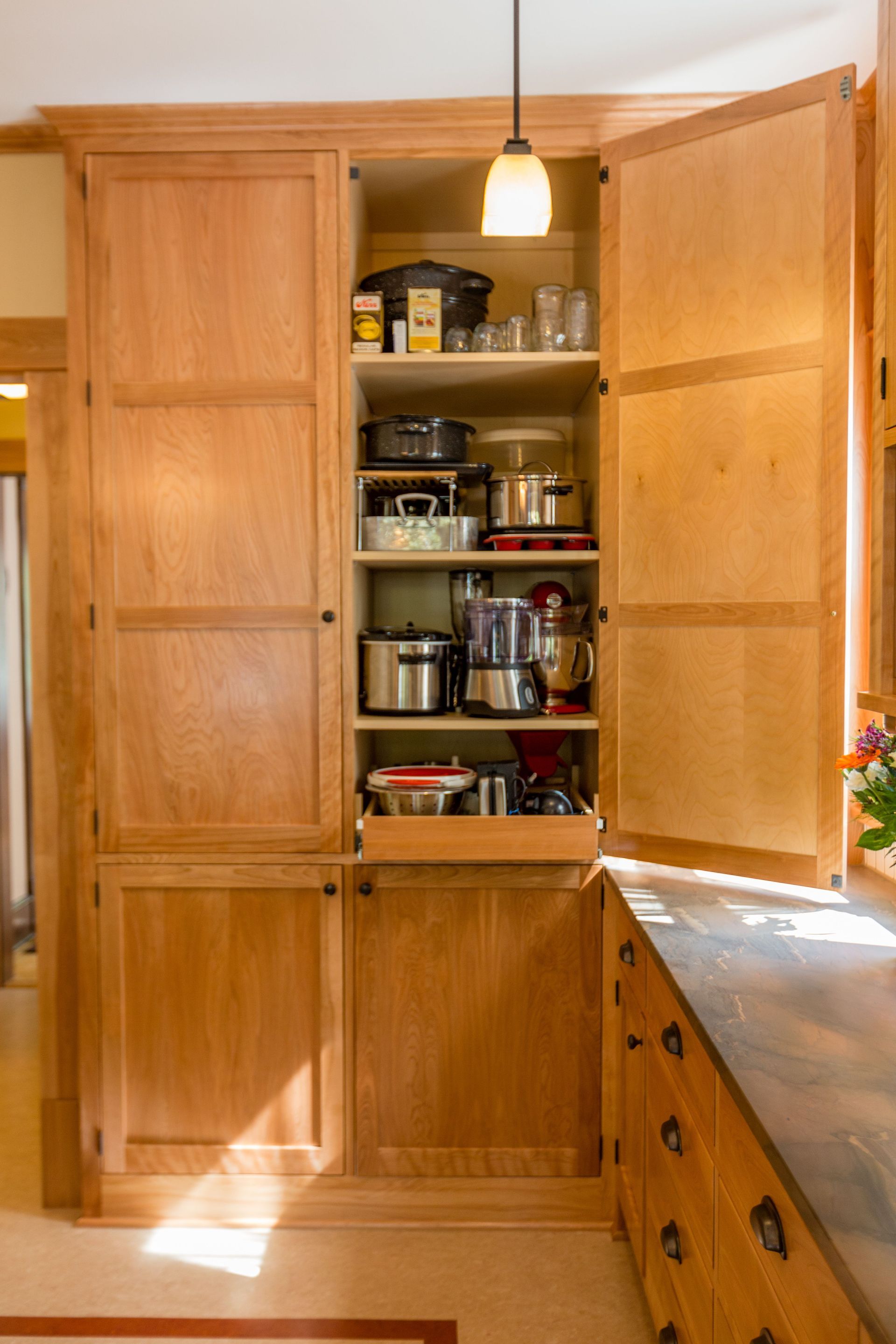 Wooden kitchen cabinet, open, revealing small appliances and shelf storage.