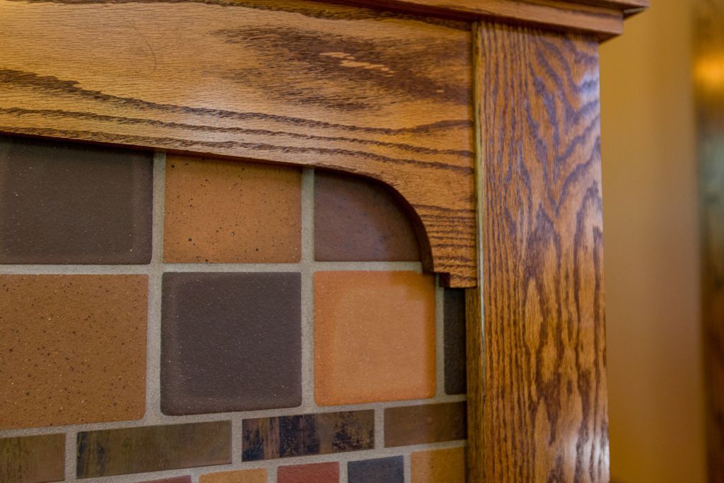Wooden fireplace mantel with decorative tiles; brown, orange, and red hues.