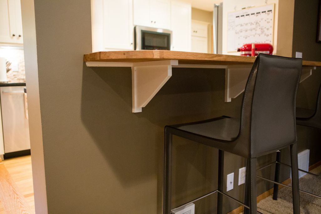 Bar with wooden countertop, white supports, and a tall chair in front.