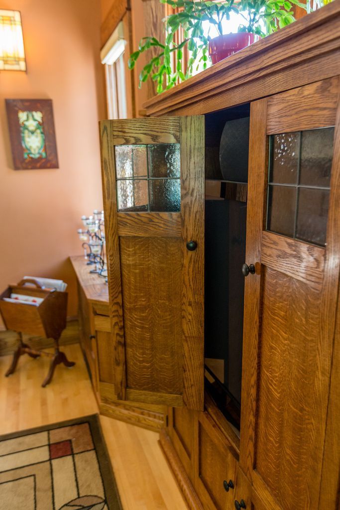 Wooden cabinet with open door, holding a dark object.  Wood floor and peach walls are visible.