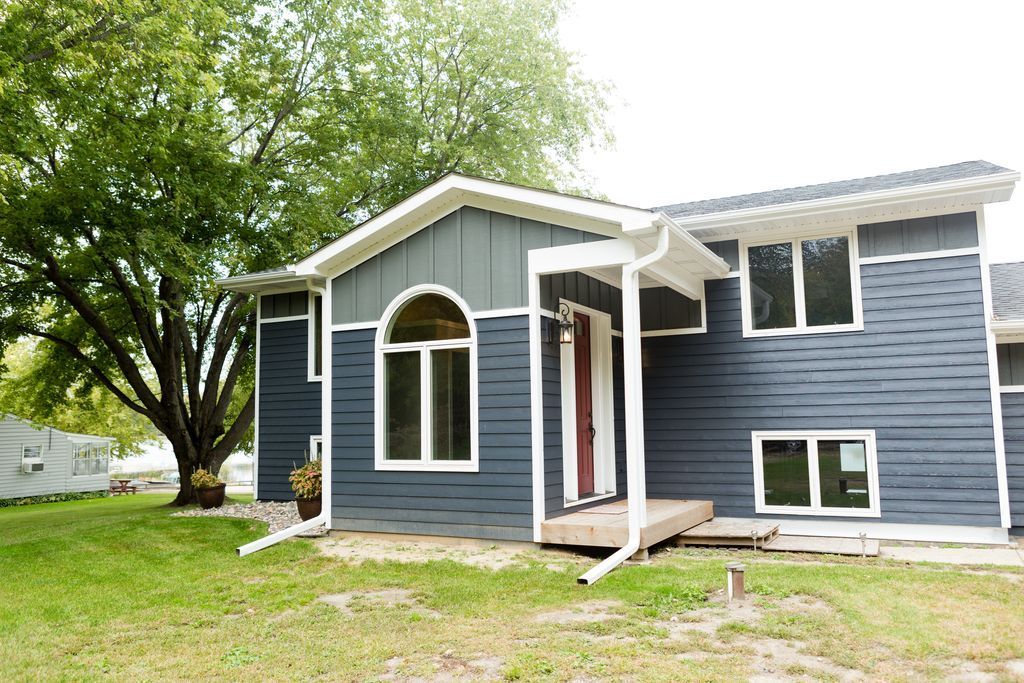 Blue house with white trim, front porch, and large tree in the yard.