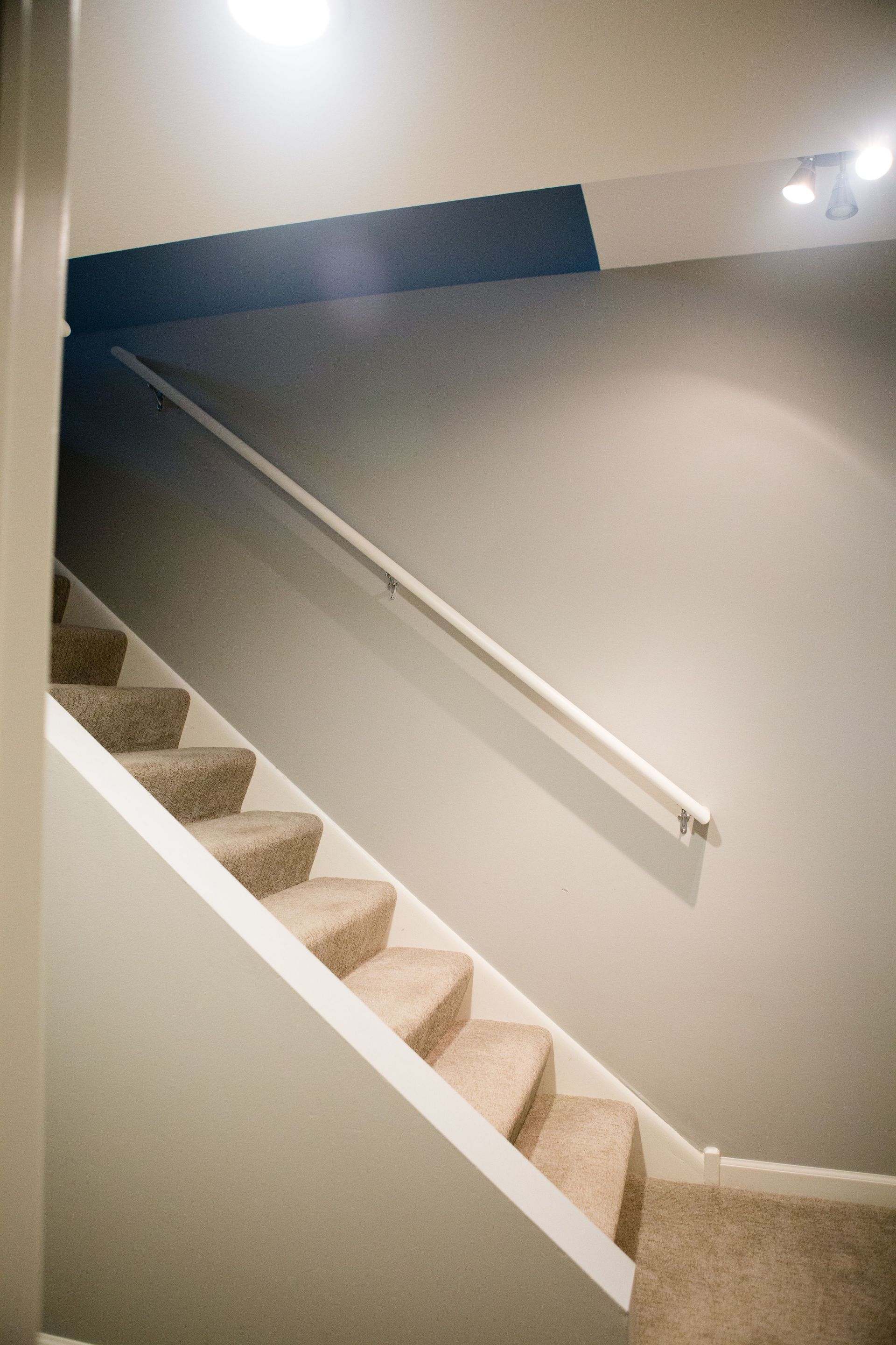 Staircase with beige carpeted steps, white trim, and handrail against a gray wall.