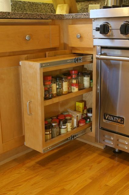Spice rack pull-out cabinet next to a stove in a kitchen with wood floors and light cabinetry.