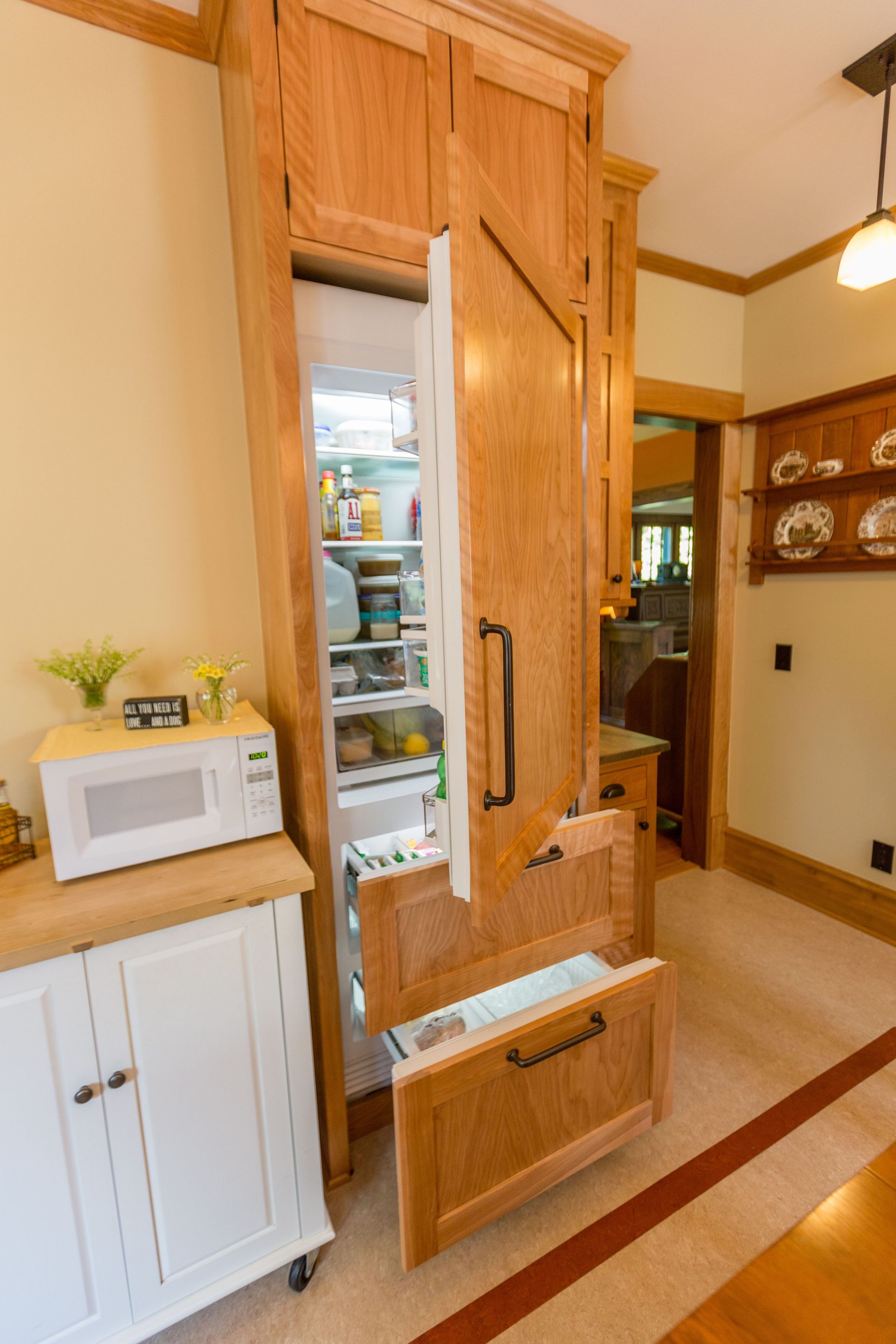 Tall, wooden built-in refrigerator with open doors, displaying shelves of food and drawers. Kitchen setting.
