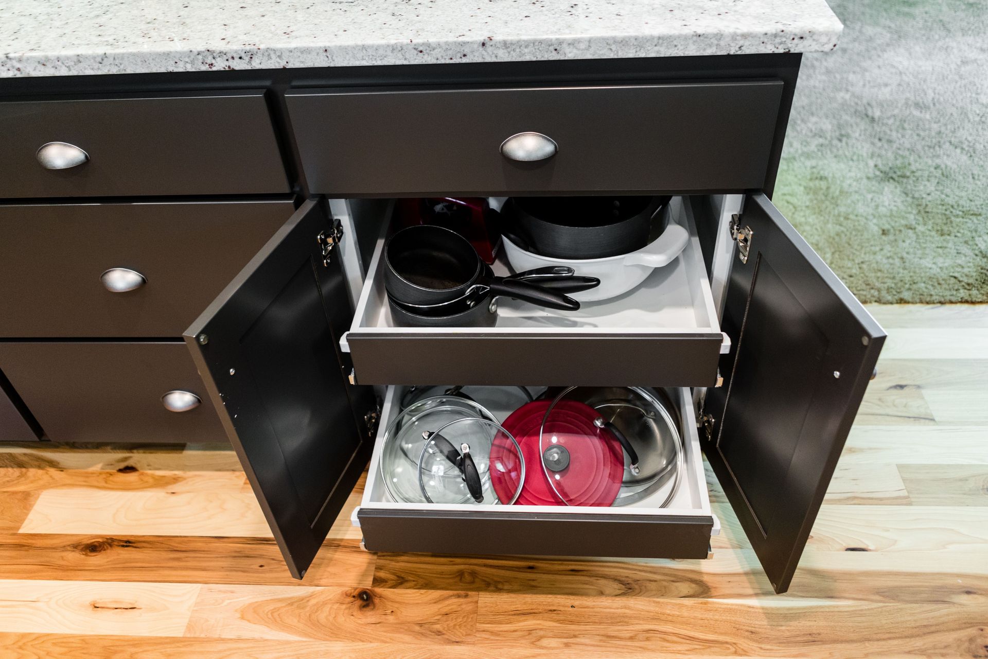 Dark kitchen cabinet with open drawers holding pots and pans.