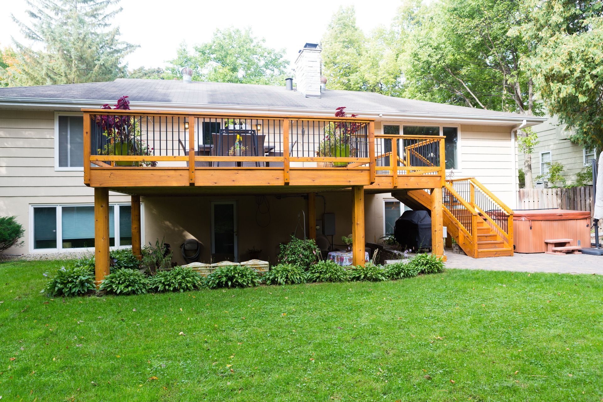 Wooden deck on a beige house, with stairs leading to a hot tub on a stone patio.
