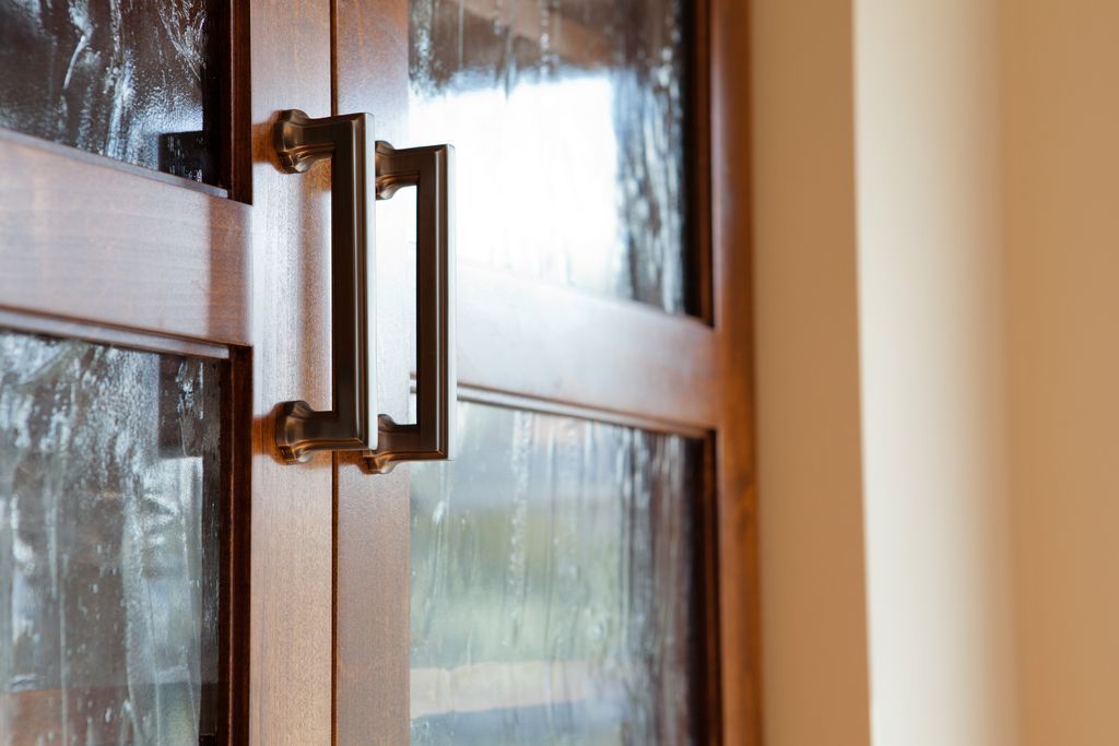 Wooden double door with decorative glass panels, bronze handles, beige wall.