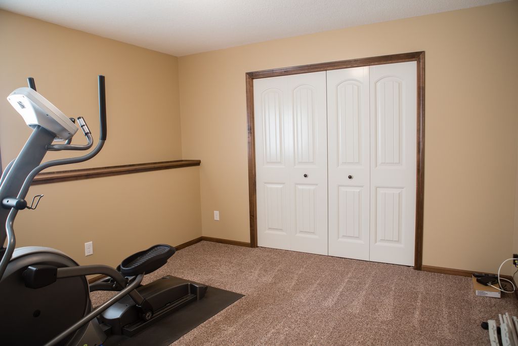 Tan exercise room with carpet, an elliptical machine, and a white closet.
