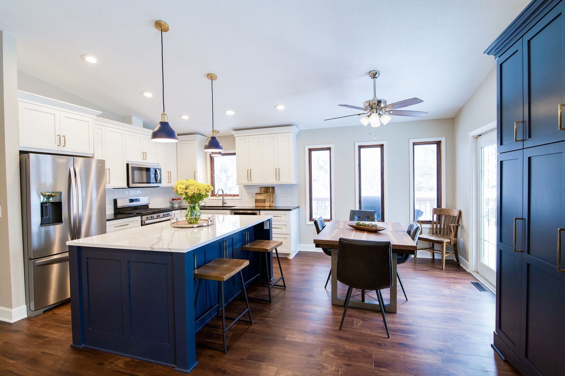 Spacious kitchen with blue island, white cabinets, stainless steel appliances, and a dining table.