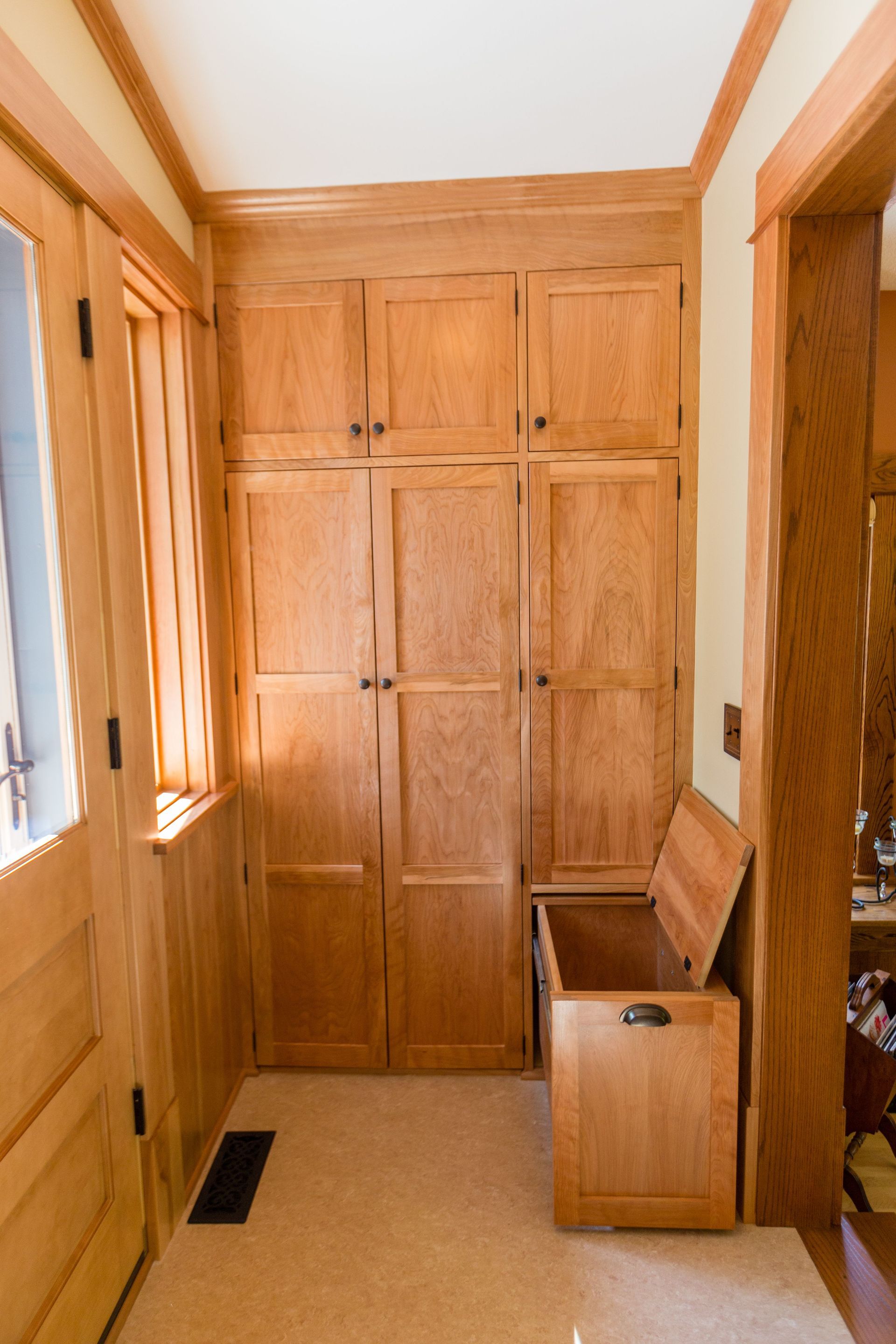 Wooden cabinet with built-in storage and a small bench in a well-lit entryway.