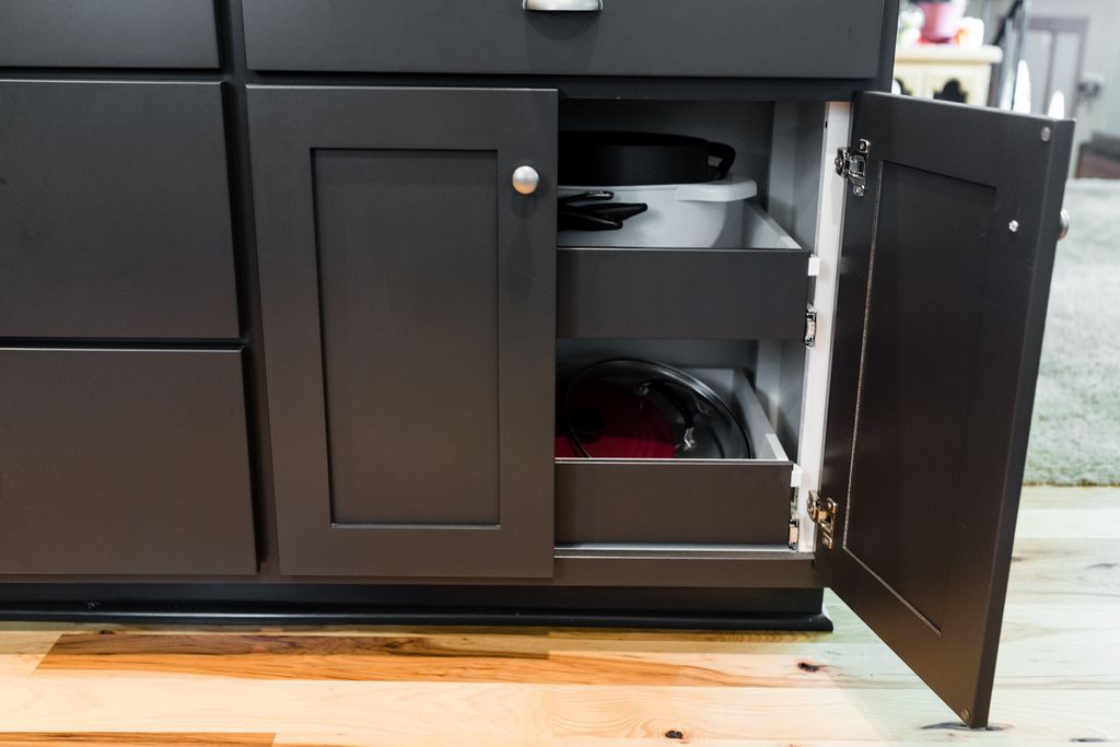 Dark gray kitchen cabinet with open door, revealing pull-out drawers containing cookware.