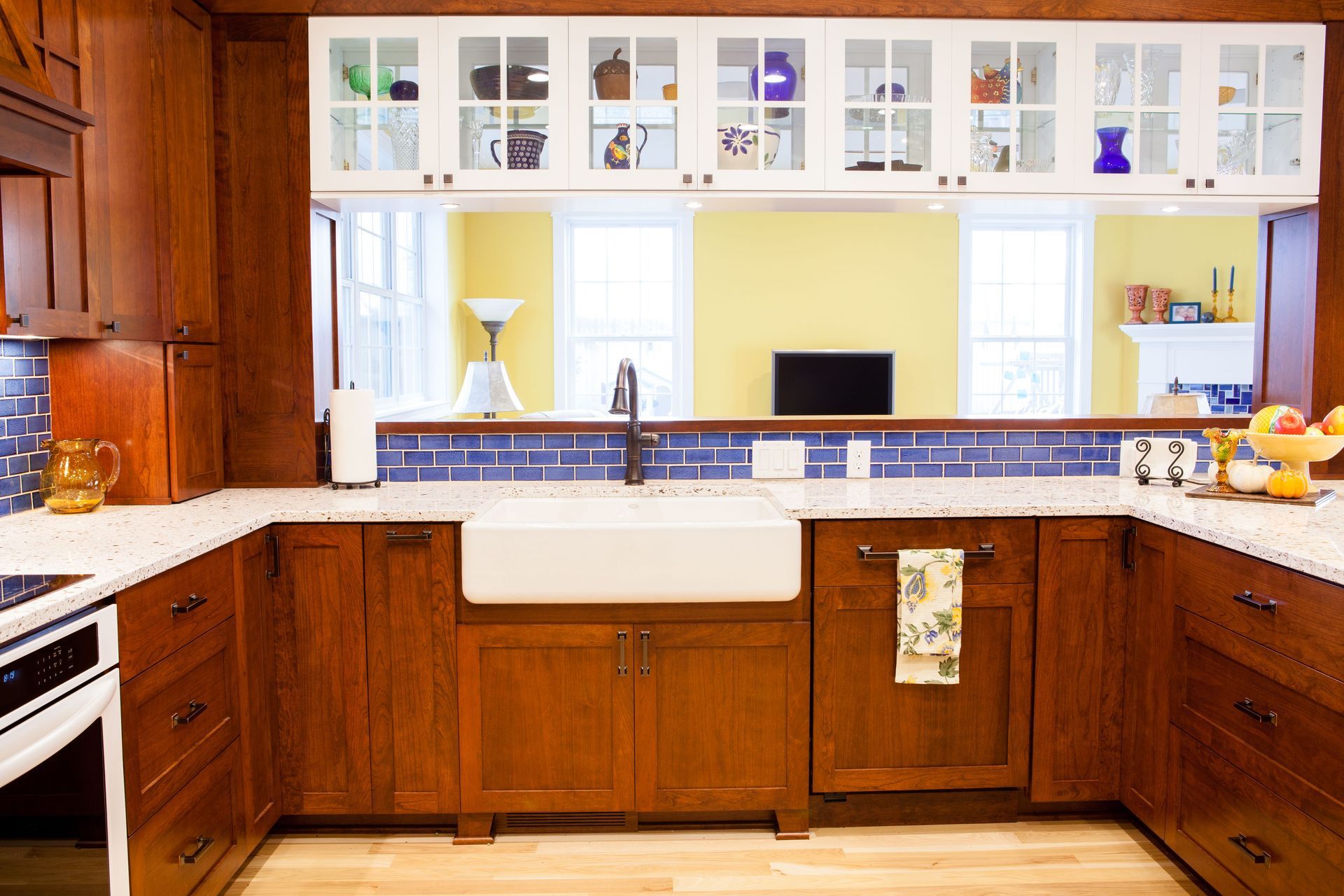 Wooden kitchen with farmhouse sink, blue tile backsplash, and glass-fronted upper cabinets displaying glassware.