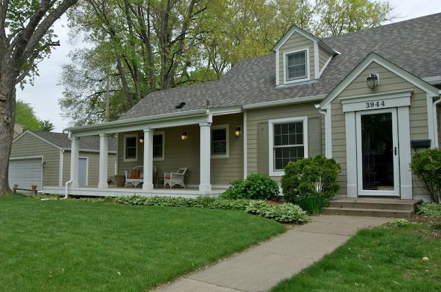 Green house with porch, white trim, green lawn, and pathway leading to the front door.