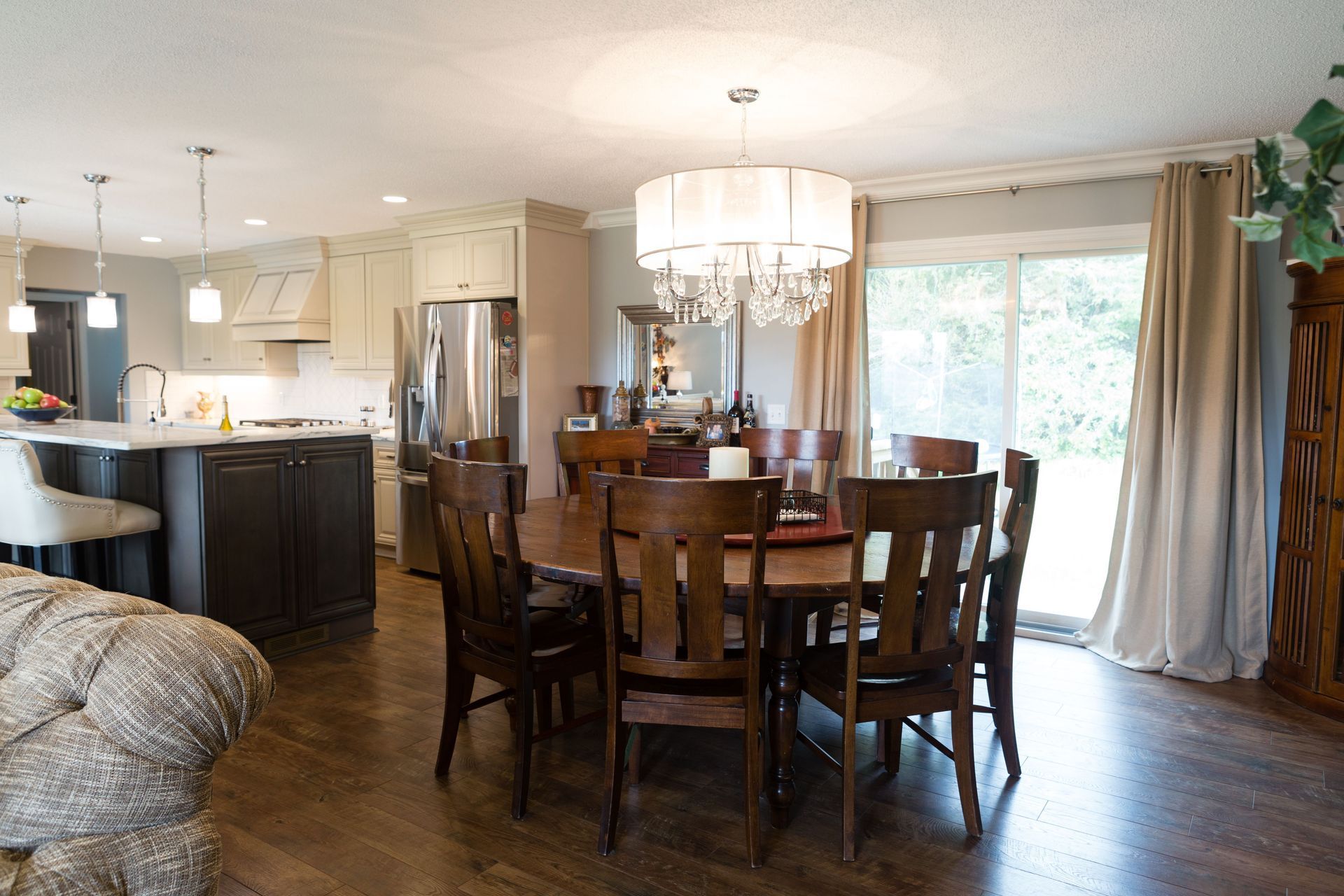Open kitchen with dining area; wood table, dark chairs, chandelier, stainless steel appliances, and sliding glass door.