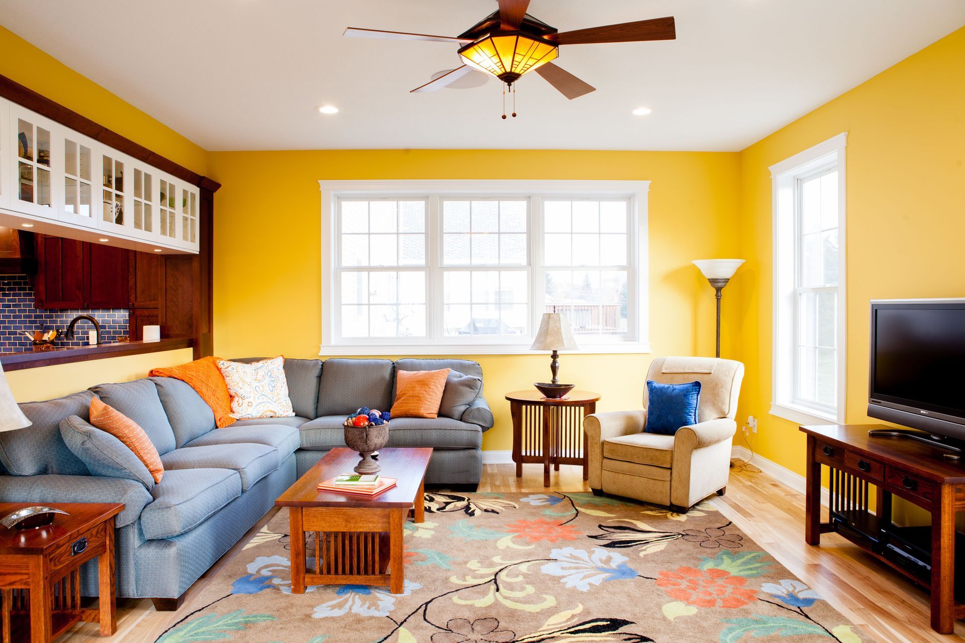 Cozy living room with yellow walls, gray sectional sofa, wooden furniture, and colorful rug.