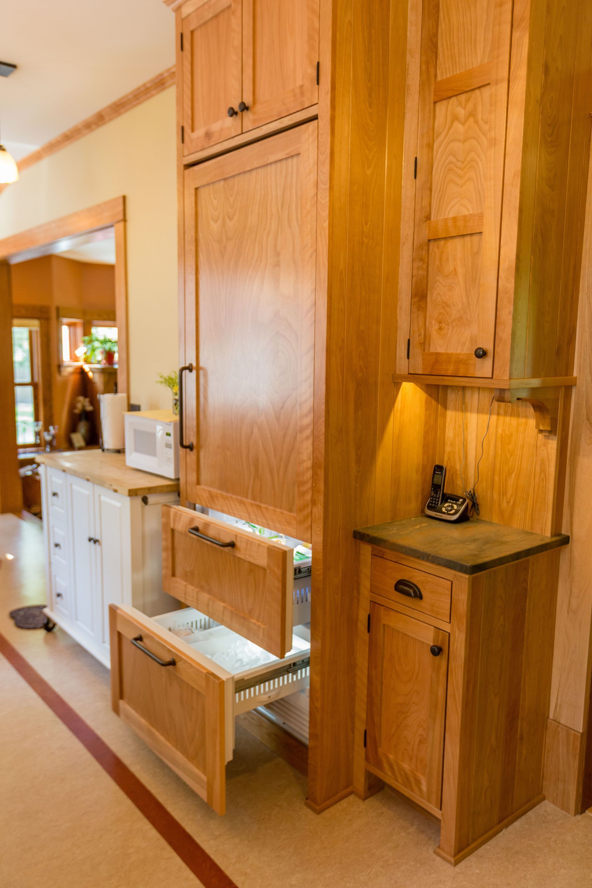 Wooden kitchen cabinetry with an integrated refrigerator and pull-out drawers, a microwave, and a small cabinet.