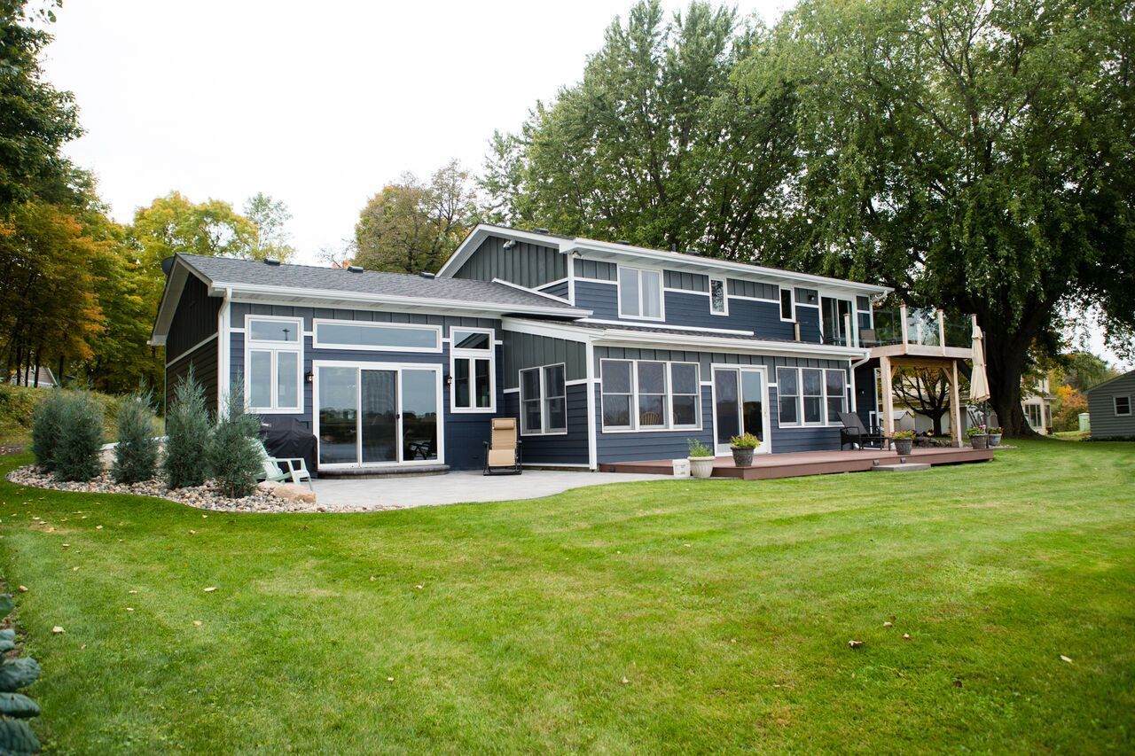 Dark blue two-story house with large windows, patio, and green lawn, with a large tree in the background.