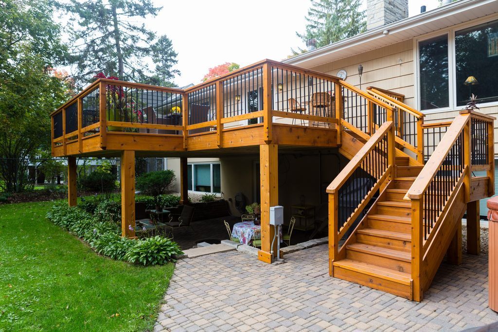 Wooden deck attached to a house with stairs, overlooking a yard.