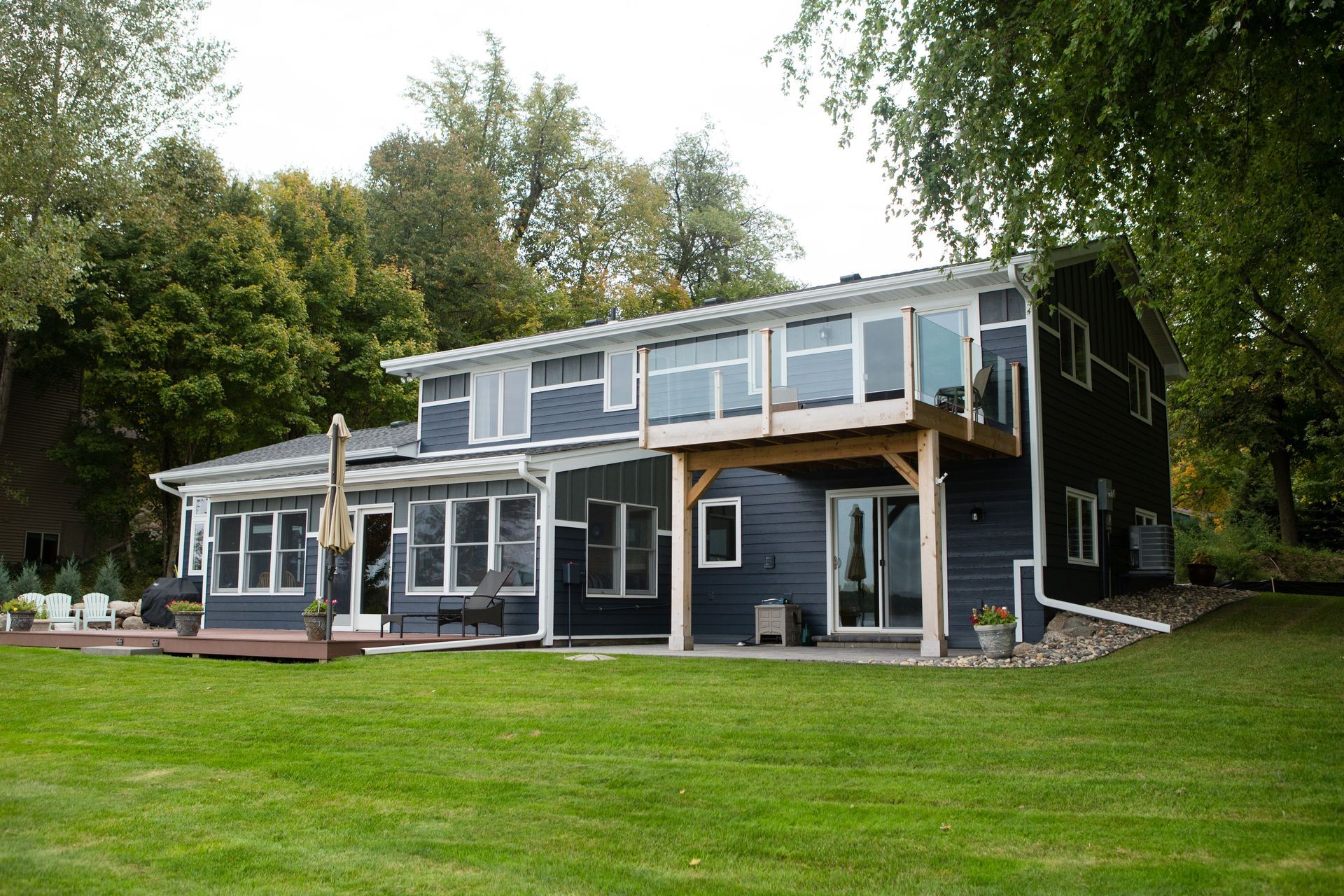 Dark blue house with a large lawn, trees, and a deck.