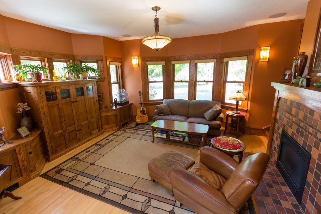 Living room with brown walls, wood furniture, sofa, chair, fireplace, and large windows.