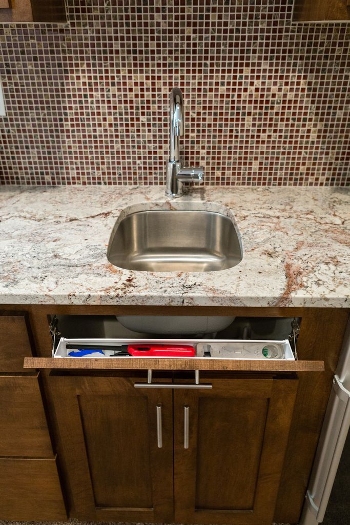 Kitchen sink with a pull-out drawer, set on a granite countertop, with a tiled backsplash.