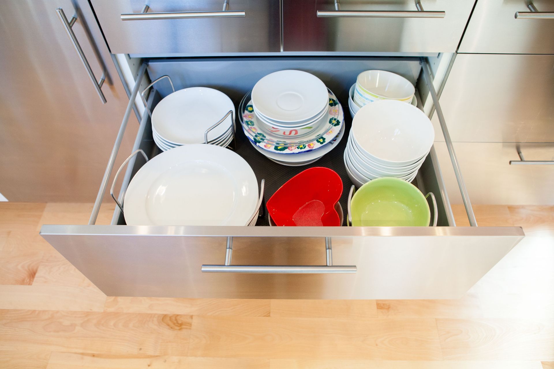 Open stainless steel kitchen drawer with plates and bowls.