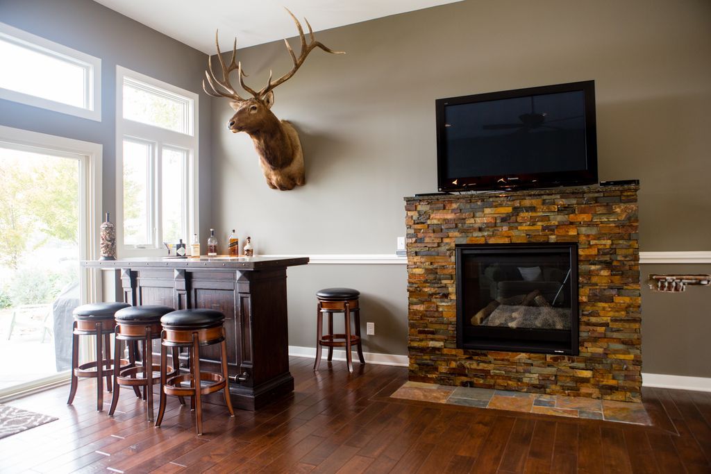 Living room with fireplace, bar, and taxidermied elk head; dark brown wood floors and stools.