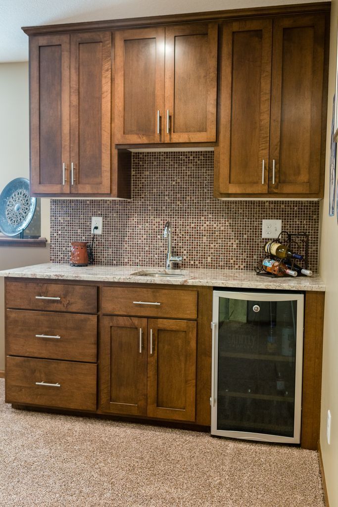 Wooden bar with cabinetry, a wine fridge, tile backsplash, and a countertop in a room.