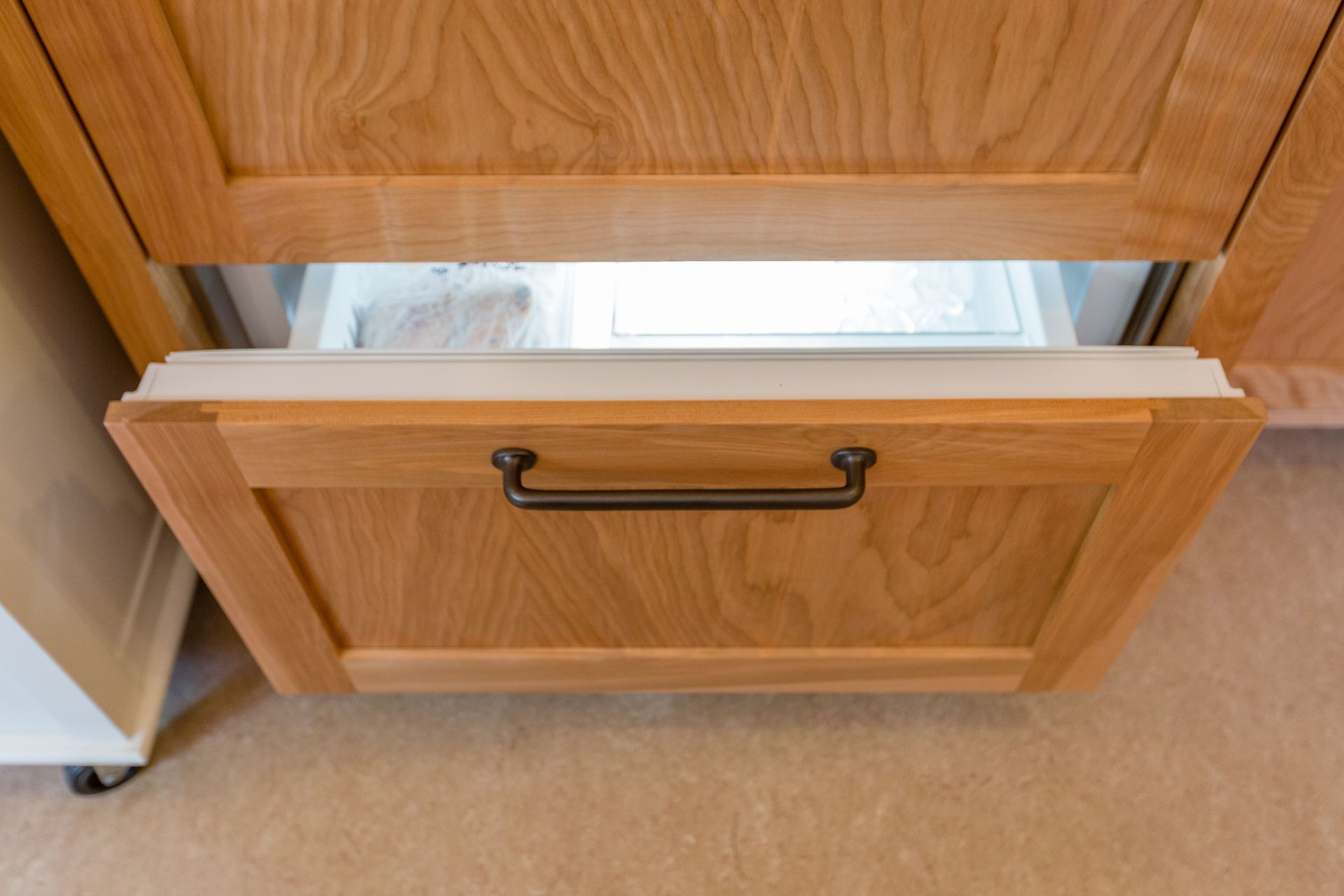 Open wooden freezer drawer with interior light on.