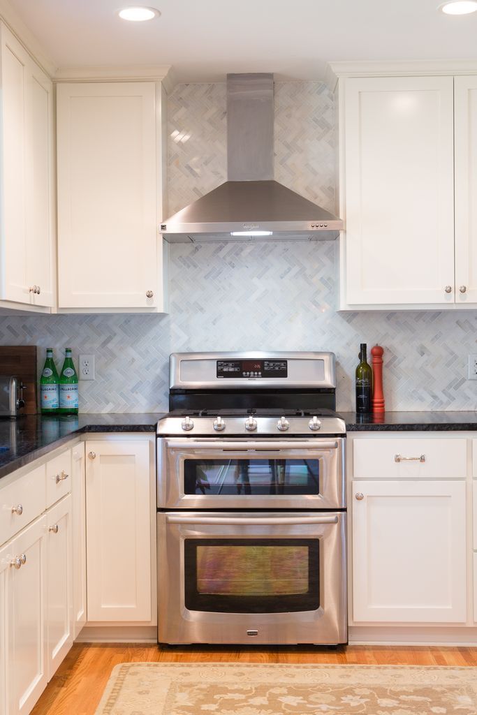 Stainless steel double oven and range with white cabinets in a kitchen with marble backsplash.